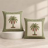 Two cream cushion covers with palm trees and green geometric borders, one on a round pedestal and one beside it
